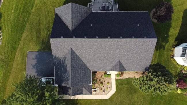 Completed residential roof installation featuring modern dark gray architectural asphalt shingles on a suburban home. The roof shows a clean, multi-gabled design with new aluminum flashing and a prominent white fascia. The image is a clear daylight photograph showcasing the quality and precision of the professional roofing services.